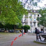 Am Brunnen vorbei sehen wir schon den Eingang des Gewerbehofs am anderen Ende des Platzes.